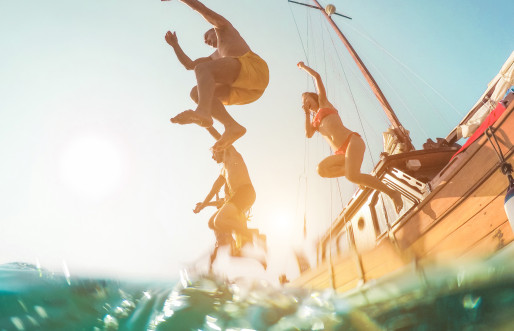 Young, diverse friends leaping from a boat into the crystal-clear sea during their vacation.